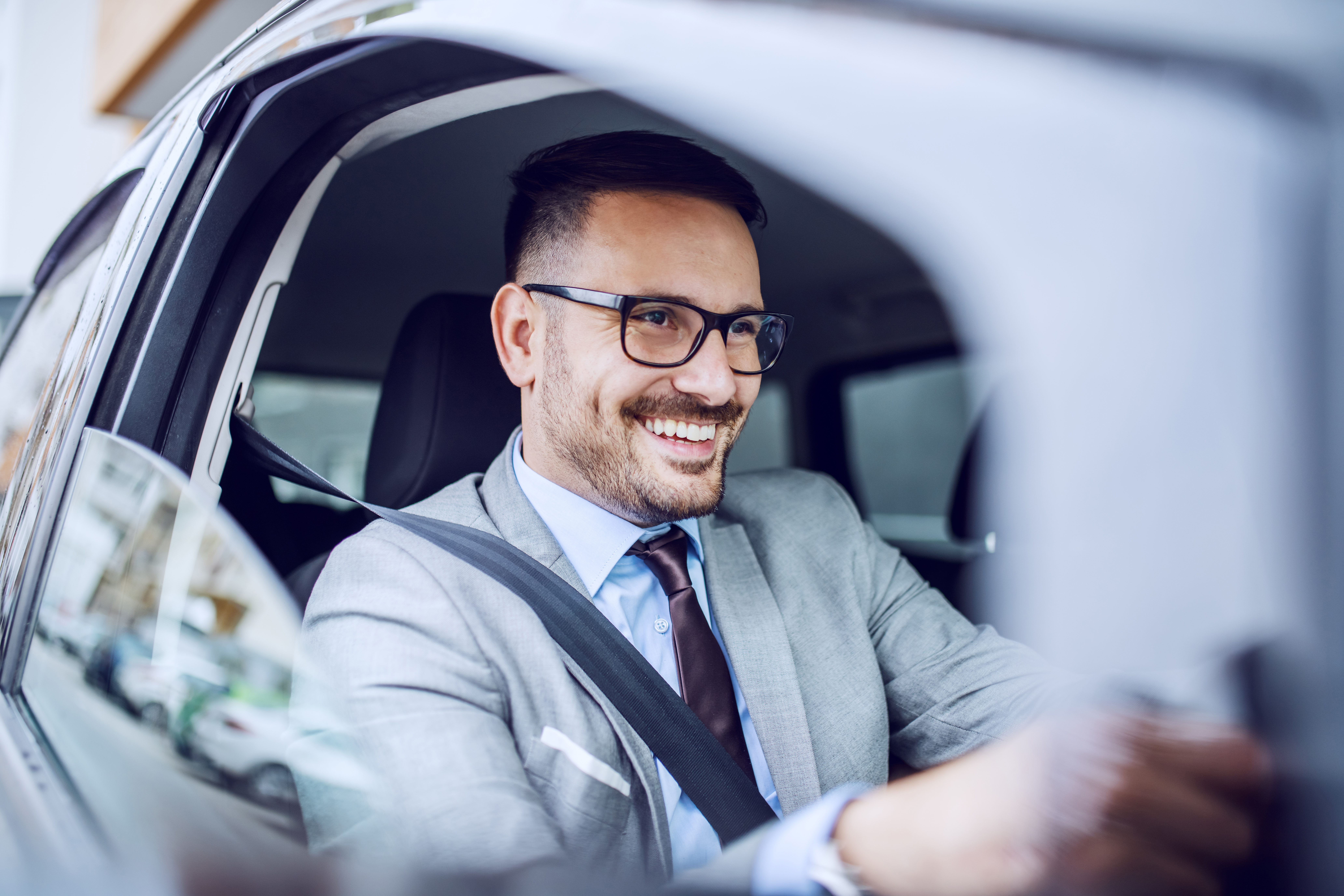 a businessman in glasses smiling driving his car