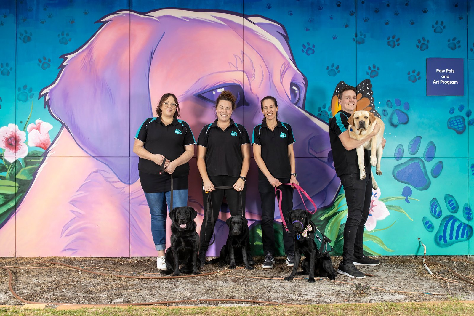 three women and one male standing and posing with a dog each